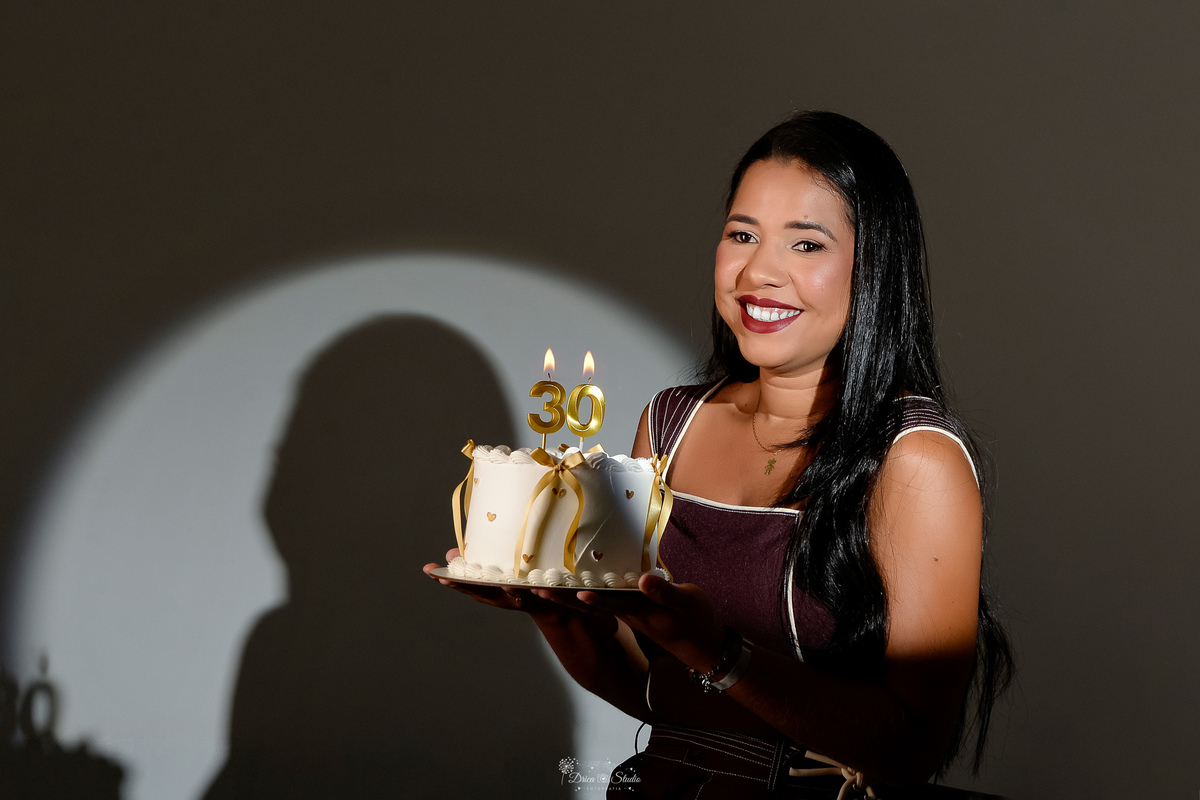 ensaio de aniversario - fotos de 30 anos - ensaio em estudio - drica studio - xinguara - pará - segurando bolo branco com laços dourados - vela de numero 30 - com luz de fundo - usando conjunto marrom - 