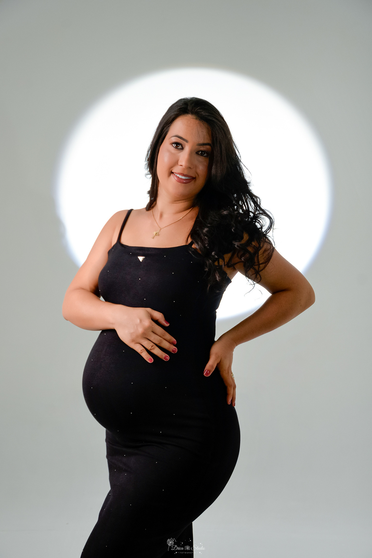 -ensaiogestante -fotografiagestante  -gravidez -maternidade - gestante usando vestido preto  com pedrinhas de brilho - com uma mão na cintura e a outra na barriga  