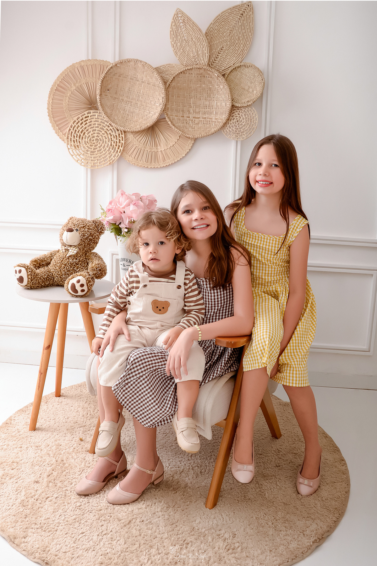 ensaio de aniversario - familia - irmãs mais velhas - 2 aninhos - fotos em estudio - drica studio - xinguara - pará - irmã mais velha sentada em poltrona - com o irmão mais novo em seu colo - irmã do meio ao lado - ursinho marrom ao lado na mesa - 