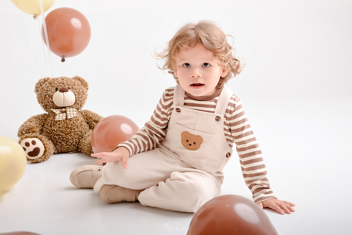 ensaio de aniversario - bebê de 2 anos - ensaio em estudio - drica studio - xinguara - pará - bebê sentado no chão usando macacão bege com camisa listrada - balões marrom ao chã - usinho de pelucia marrom - 