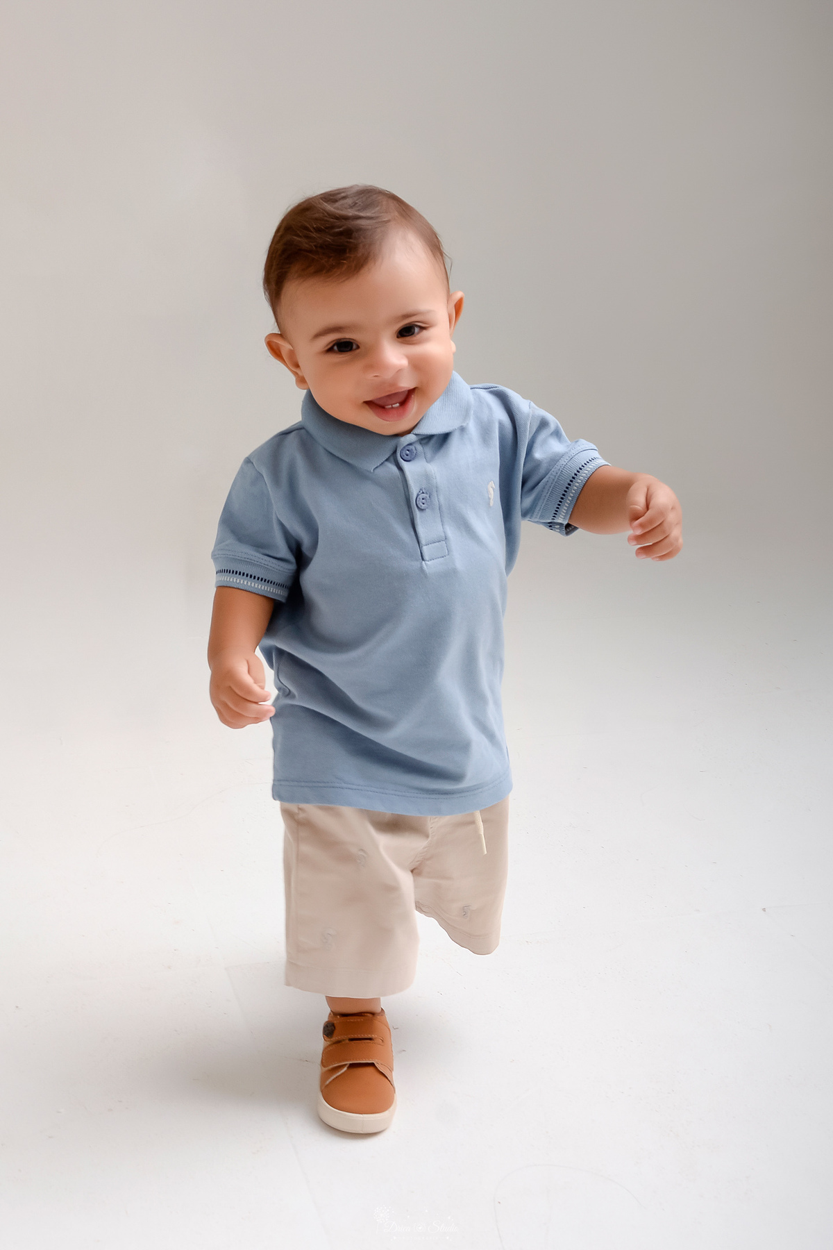 Drica studio - ensaio infantil - ensaio de 1 ano - smash the cake - arca de noé - acompanhamneto mensal - bebe dando seus primeiros pasinhos em seu ensaio de 1 ano - usando camisa gola polo azul claro e bermuda bege - 