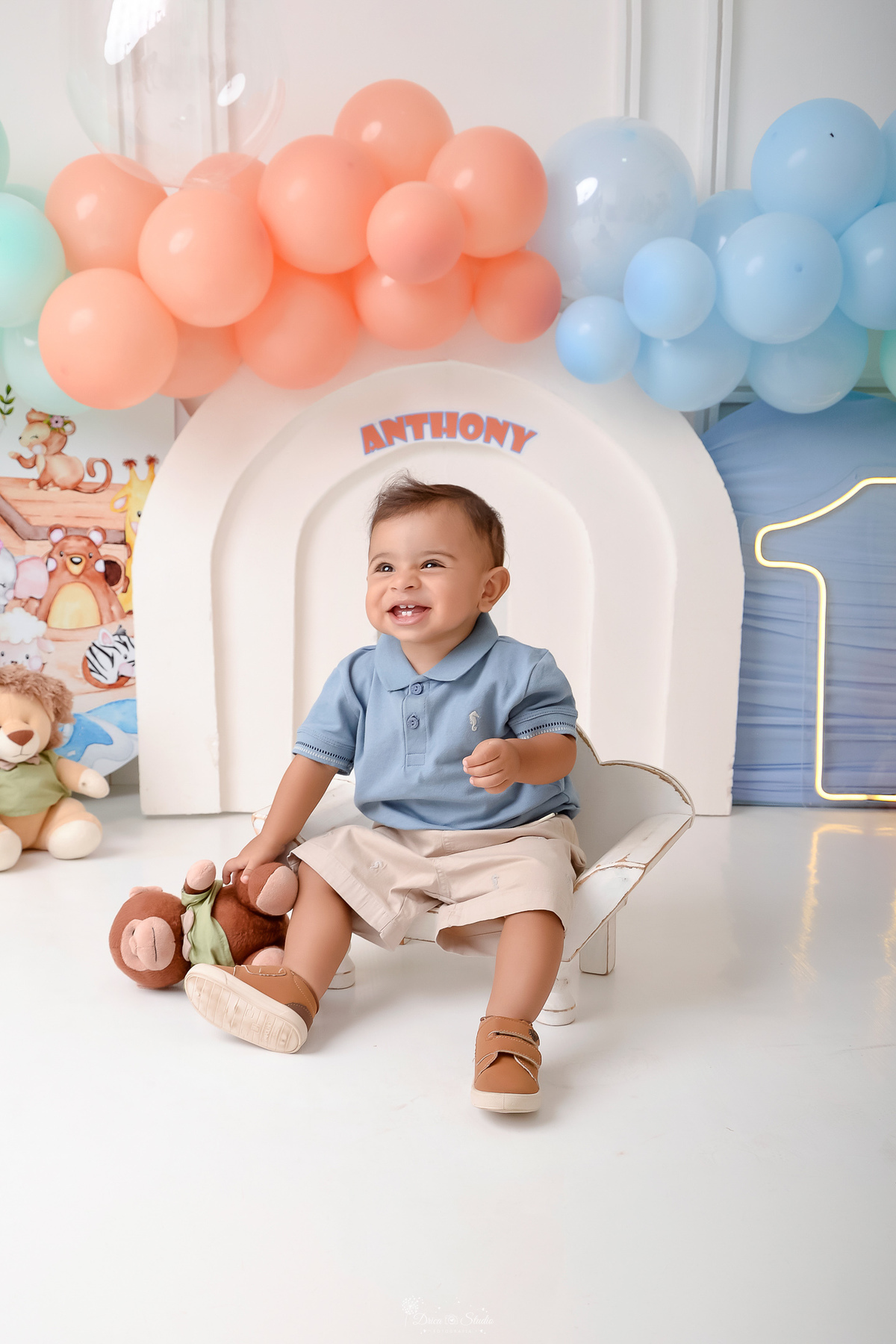 Drica studio - ensaio infantil - ensaio de 1 ano - smash the cake - arca de noé - acompanhamneto mensal - cenario de arca de noé - bebe sentado em baquinho de madeira branco - 1 de led - bebe usando camisa gola polo azul claro e bermuda bege - 