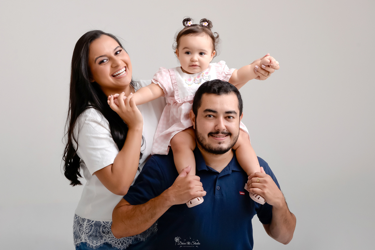 Drica studio - smash the cake - ensaio familia - 1 aninho - ensaio em estúdio - mãe, pai e filha - filha sobre as costas do papai, mãe segurando as mãozinhas da filha - foto com fundo branco 