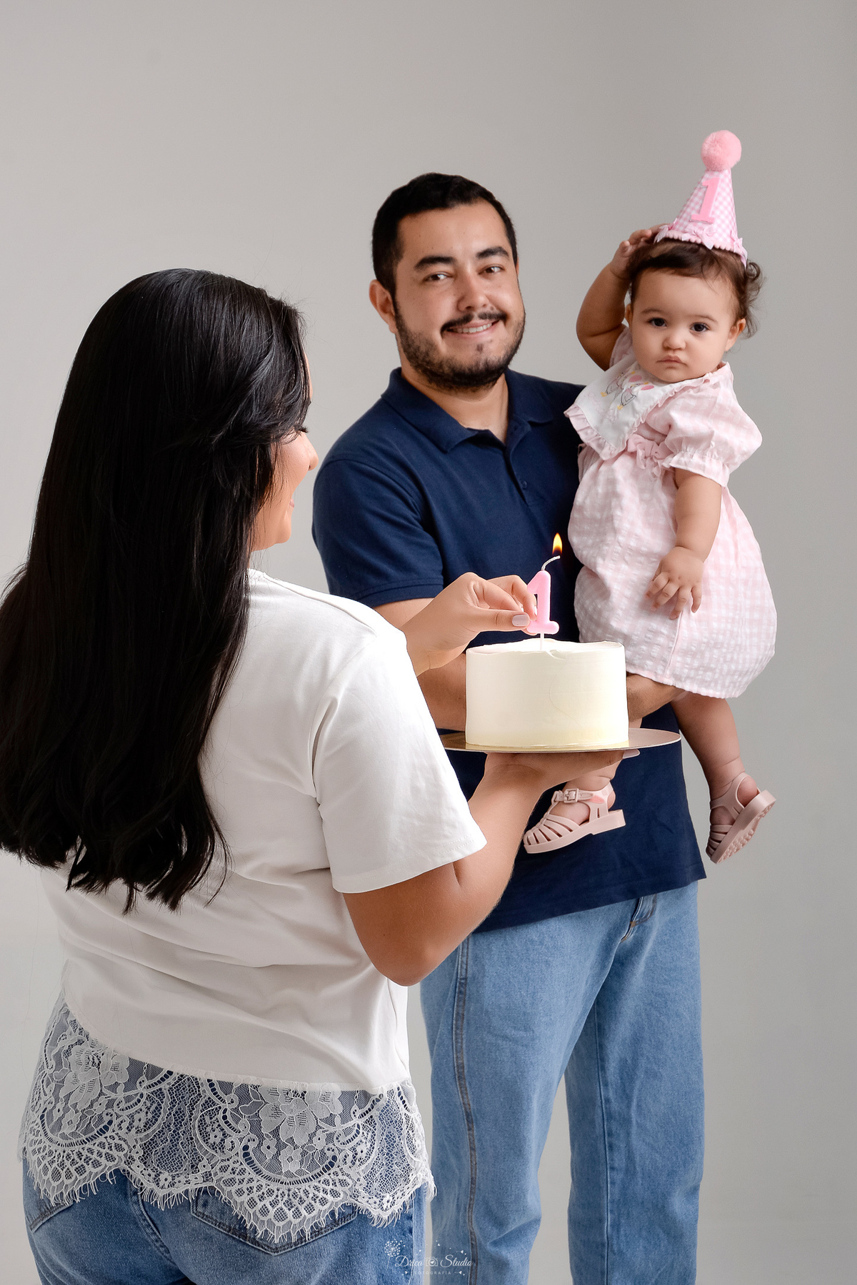 Drica studio - smash the cake - ensaio familia - 1 aninho - ensaio em estúdio - mãe colocando a vela no bolo - pai segurando a filha no colo - 