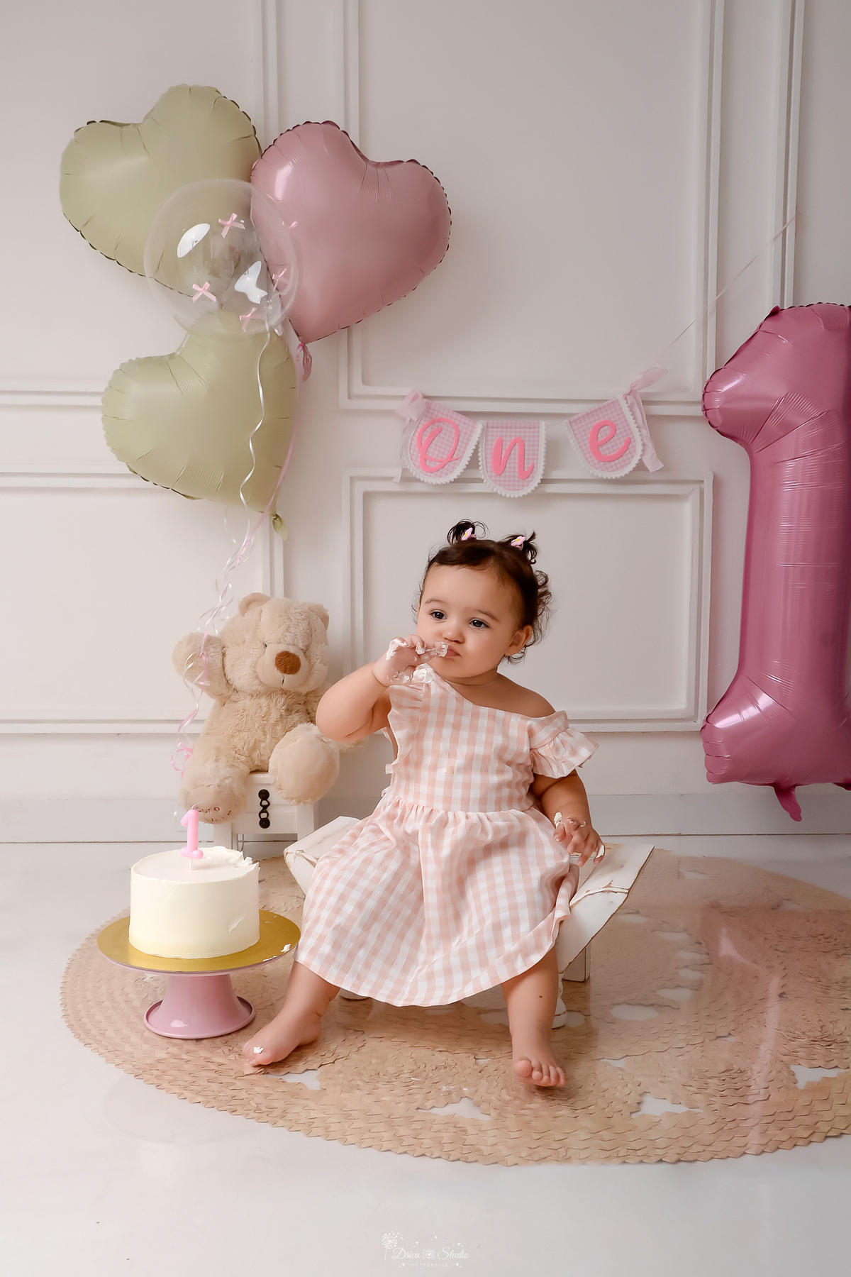 Drica studio - smash the cake - ensaio familia - 1 aninho - ensaio em estúdio - bebe sentada em baquinho de madeira branco - ursinho de pelucia ao fundo segurando balões - one na parede - balão de numero 1 - bebe esperimentando o bolo - vela de numero 1 