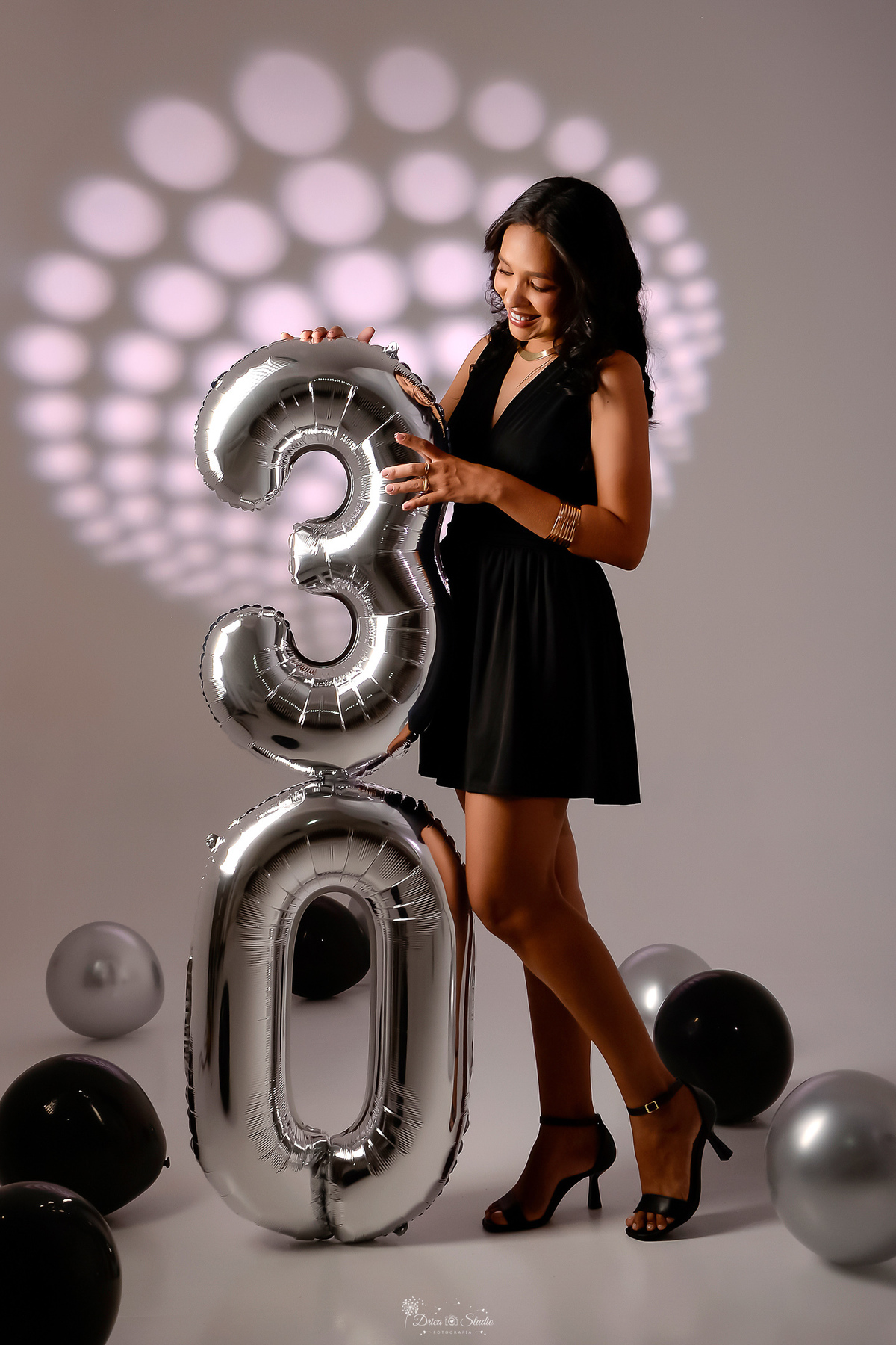 drica studio - xinguara - pará - ensaio de aniversário - 30 anos - trintou - fotos em estudio - usando vestido preto - segurando balões de numero 30 um numero em cima do outro - balões pretos e pratas espalhados no chão - ao fundo luz de led 