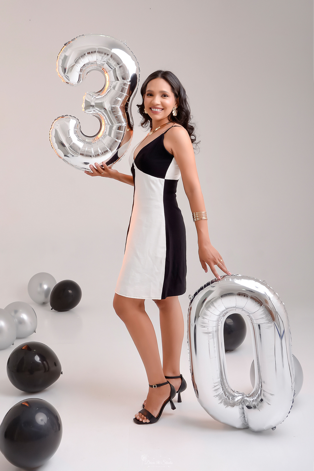drica studio - xinguara - pará - ensaio de aniversário - 30 anos - trintou - fotos em estudio - usando vestido preto e branco - com balões de numero 30 - balões pretos e pratas espalhados pelo chão - foto com fundo branco -