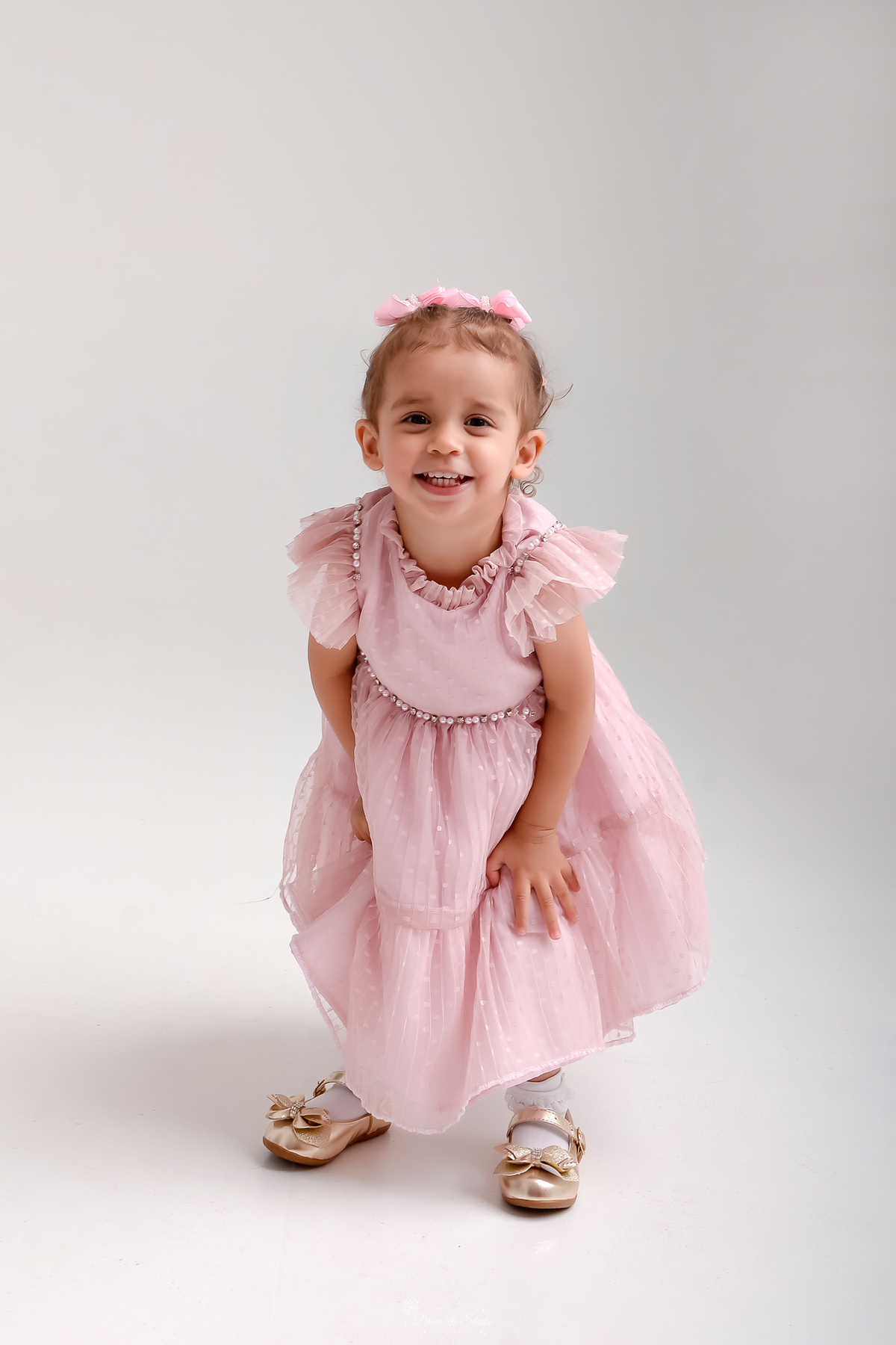 Drica studio - ensaio familia - ensaio de 2 anos - fotos em estudio - bebê de 2 aninho - usando vestido rosa - com laçoes rosas na cabeça - fazendo pose e sorrindo para a foto - foto com o fundo branco - 
