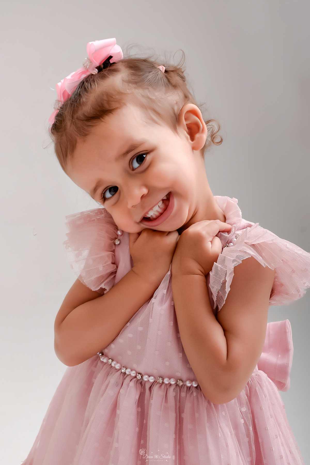 Drica studio - ensaio familia - ensaio de 2 anos - fotos em estudio - bebê de 2 aninhos - usando vestido rosa - com laços rosas na cabeça - foto com fundo branco - bebê com as mãozinhas no rosto - sorrindo para a foto -