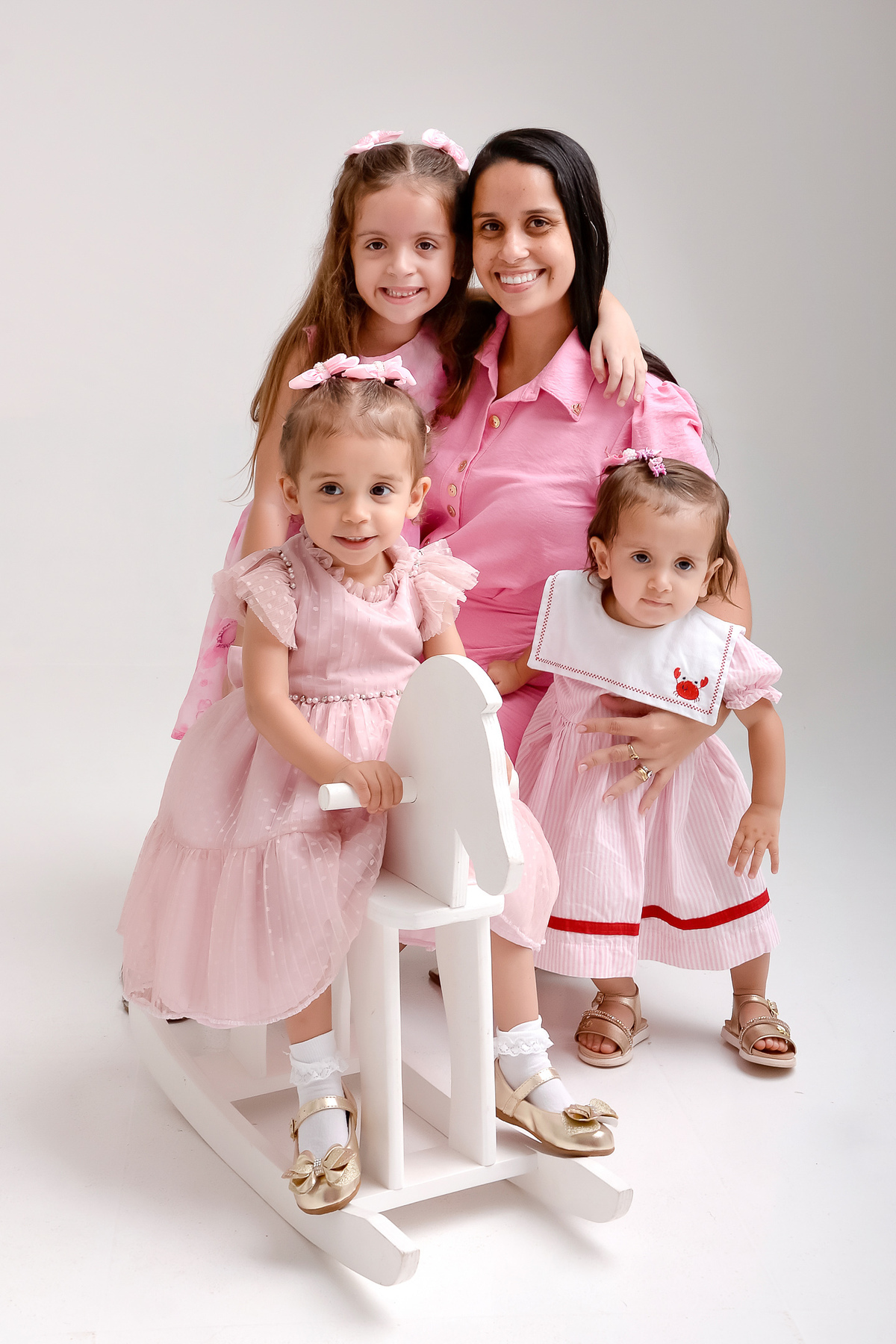Drica studio - ensaio familia - ensaio de 2 anos - fotos em estudio - tia com sua sobrinha e sua filha - as 3 usando vestidos rosas - bebê de 2 aninhos em cavalinho de madeira branco - 