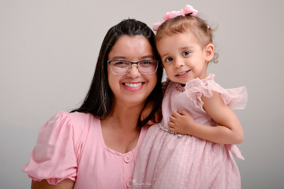 Drica studio - ensaio familia - ensaio de 2 anos - fotos em estudio - avó e neta - usando vestidos rosas - foto com fundo branco - neta usando laços rosas no cabelo
- 