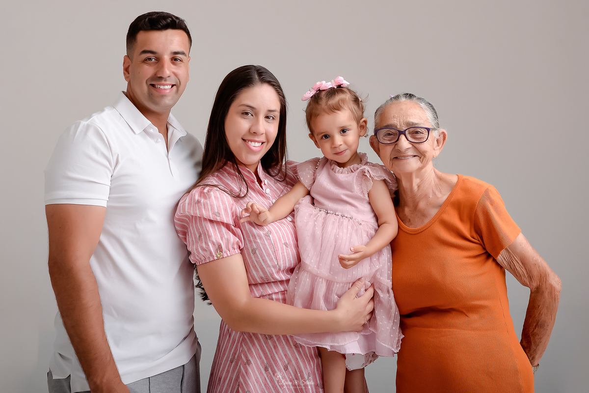Drica studio - ensaio familia - ensaio de 2 anos - fotos em estudio - pai, mãe, filha e bisavó - mãe e filha usando vestidos rosas - pai usando camisa branca - bisavó usando vestido laranja - foto com o fundo branco - 