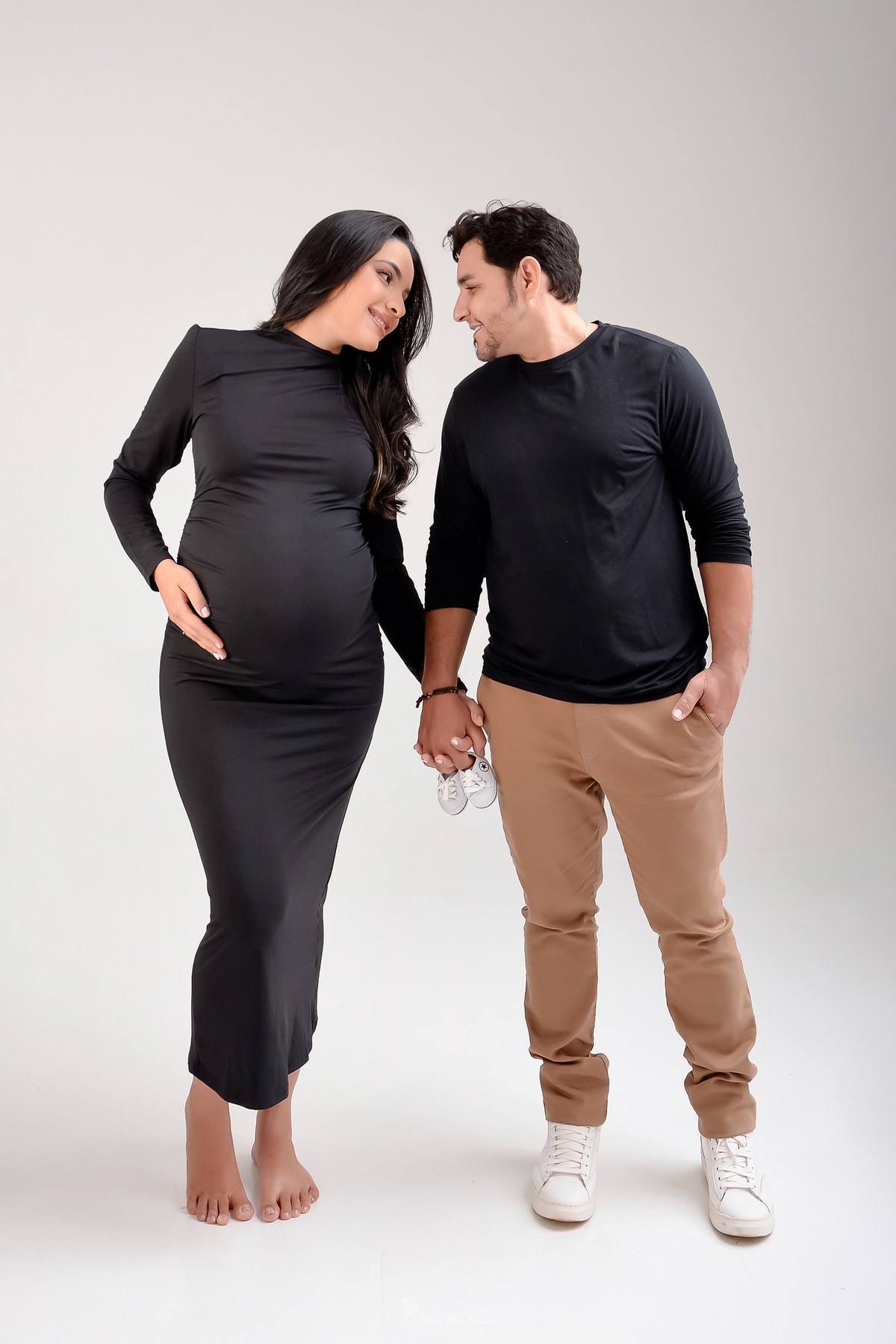 drica studio - xinguara- pará - ensaio gestante - mamãe de primeira viagem - fotografia de gestante - baby boy - papai e mamãe - mamãe usando vestido de manga longa preto - pai usando camisa preta e calça bege - segurando sapatinho do bebê 