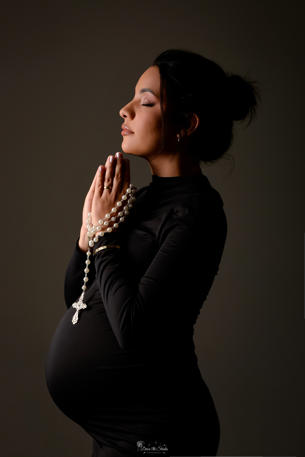 drica studio - xinguara- pará - ensaio gestante - mamãe de primeira viagem - fotografia de gestante - baby boy - mãe usando vestido de manga longa na cor preta - segurando terço nas mãos 