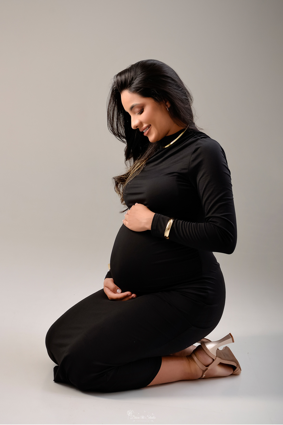 drica studio - xinguara- pará - ensaio gestante - mamãe de primeira viagem - fotografia de gestante - baby boy - mamãe sentada sobre um baquinho usando vestido preto manga longa - com as mãos sobre a barriga - foto em fundo branco -