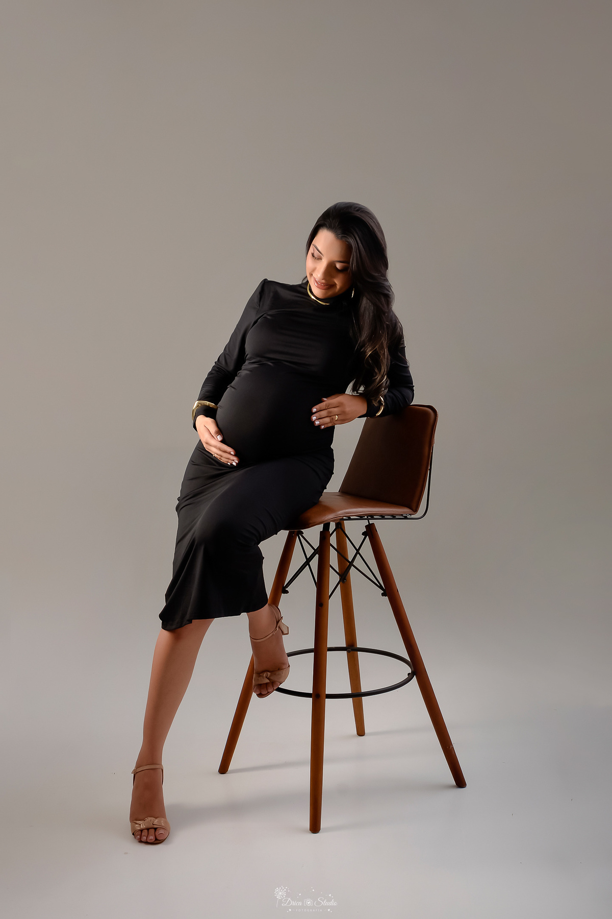 drica studio - xinguara- pará - ensaio gestante - mamãe de primeira viagem - fotografia de gestante - baby boy - papai e mamãe - mãemãe sentada em cadeira - usando vestido preto manga longa- com as mãos sobre a barriga - 
