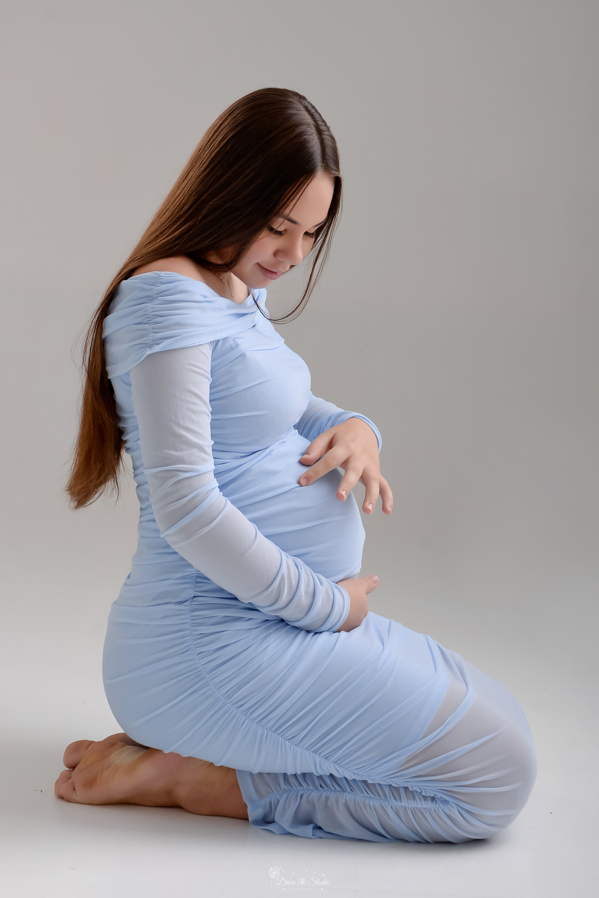 Ensaio gestante - ensaio em estudio - mamãe de primeira viagem - drica studio - xinguara - pará -  mamãe usando vestido azul - sentada sobre o chão - com as mãos na barriga - 