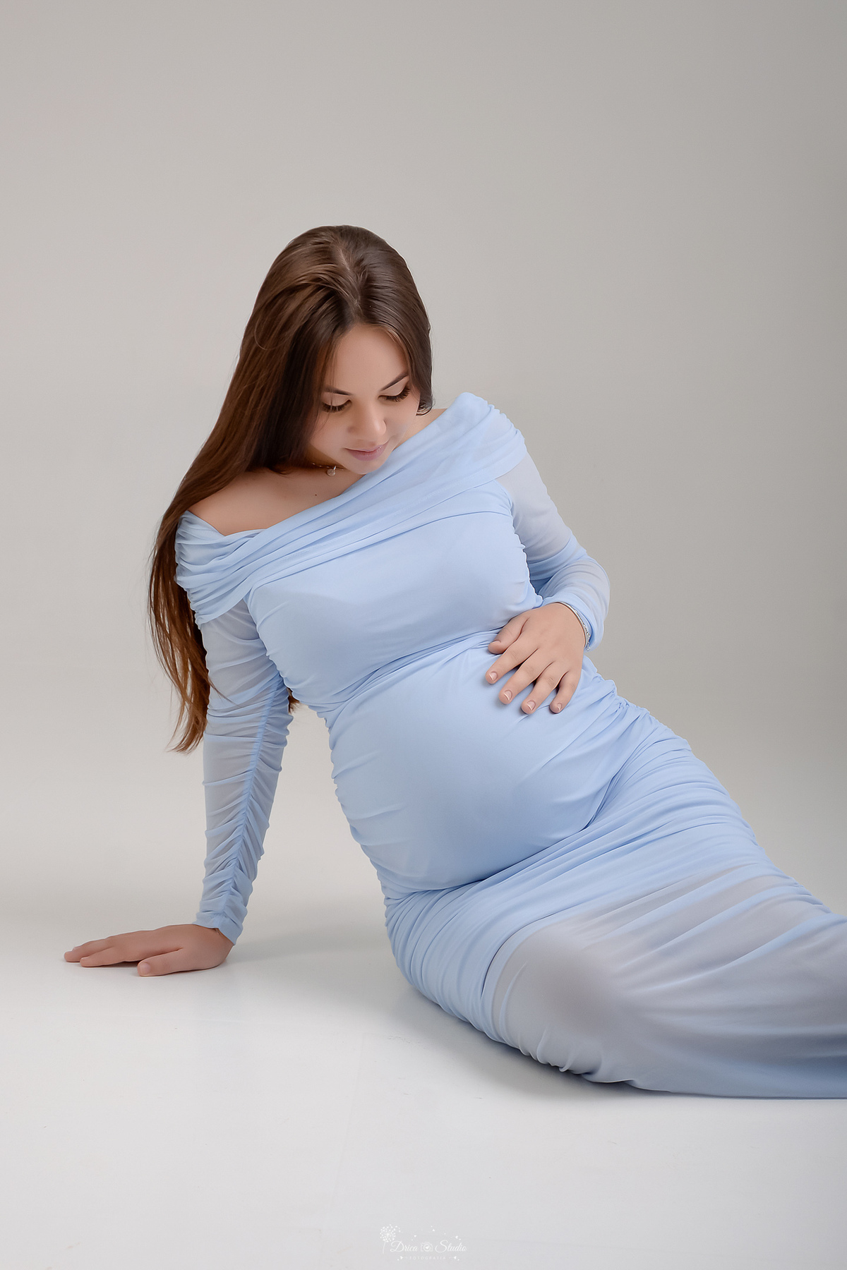 Ensaio gestante - ensaio em estudio - mamãe de primeira viagem - drica studio - xinguara - pará  mamãe usando vestido azul - sentada sobre o chão - com as mãos na barriga - 