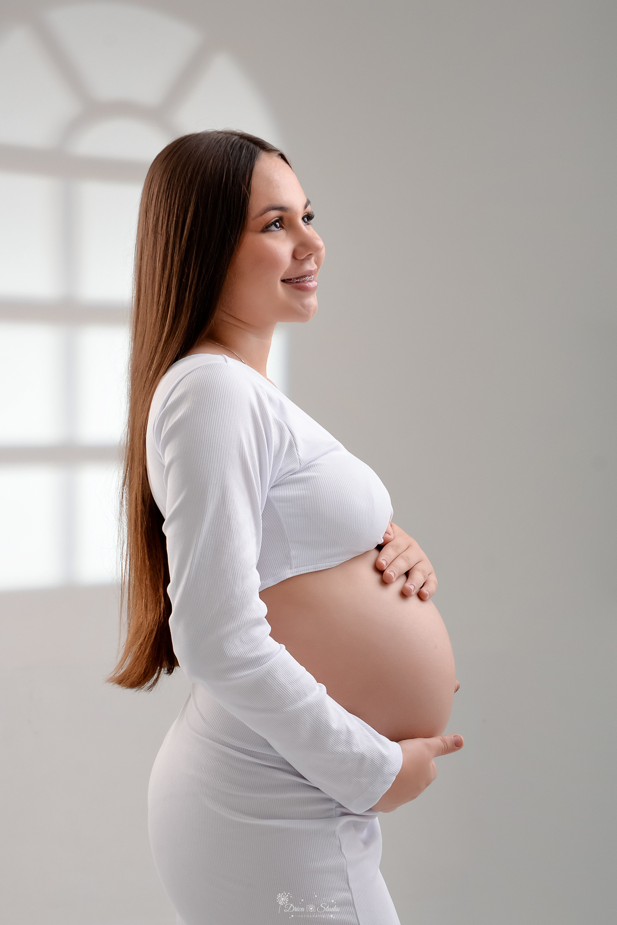 Ensaio gestante - ensaio em estudio - mamãe de primeira viagem - drica studio - xinguara - pará - mamãe usando vestido branco - com as mãos sobre a barriga - olhando para o lado 