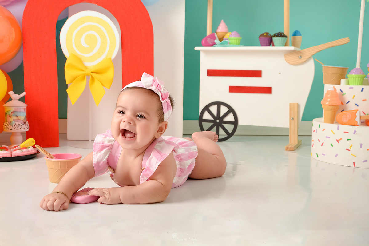ompanhamento mensal - dia das crianças - cenário doce - mês das crianças - cenário com tematica doce - bebe deitada sobre o cenário - usando roupinha rosa - sorrindo para a foto - 