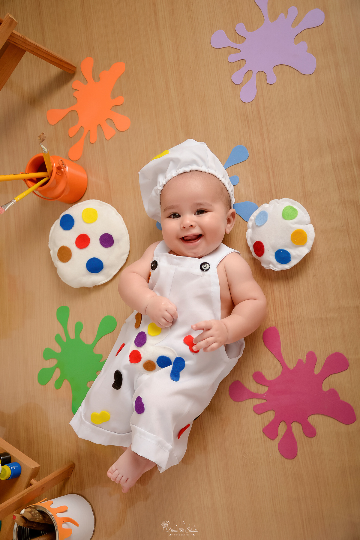 acompanhamento infantil - cenário de aquarela - dia das crianças - mês das crianças - cenários com latas de tintas - bebe deitado sobre o cenário ao lado de lata de tintas 