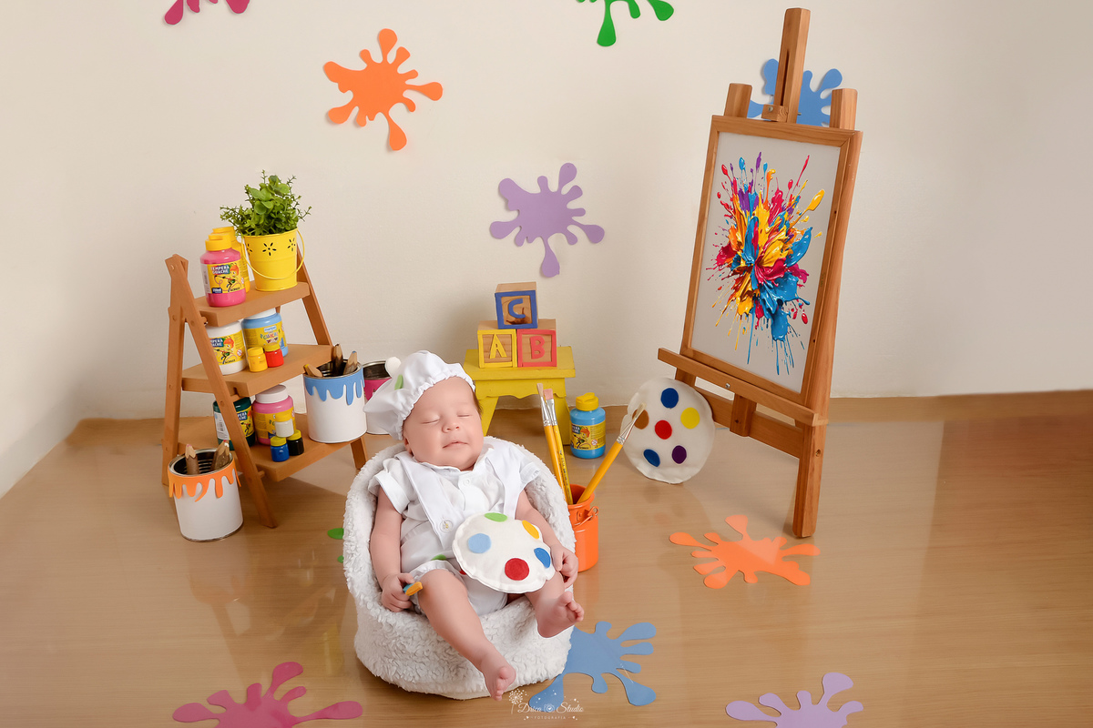 acompanhamento infantil - cenário de aquarela - dia das crianças - mês das crianças - cenários com latas de tintas - bebe dormindo em mini sofazinho - com roupinha de pintor e gorrinho na cabeça - lousa de pintura ao lado - pincéis de pintura 