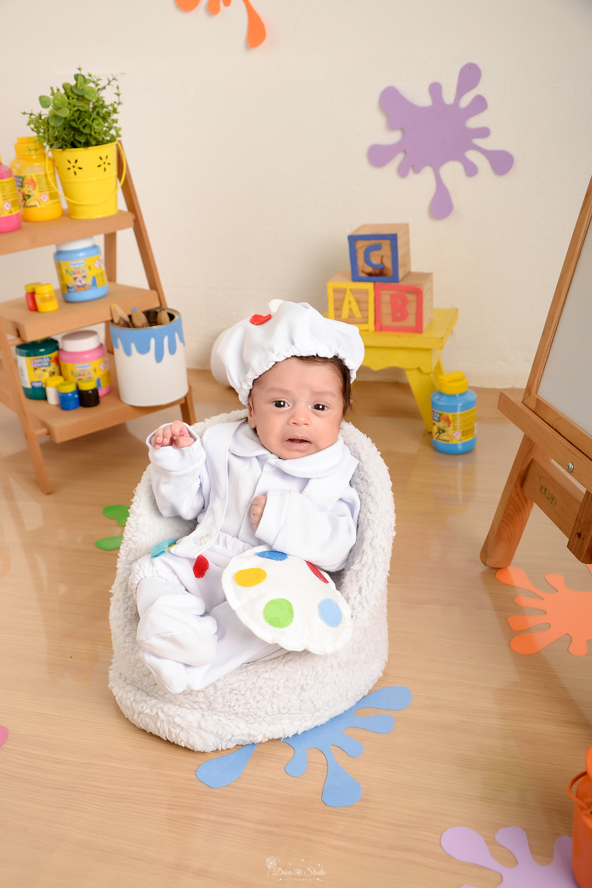 acompanhamento infantil - cenário de aquarela - dia das crianças - mês das crianças - cenários com latas de tintas - bebe sentado em mini sofazinho - usando roupinha de pintor e gorrinho na cabeça - 
