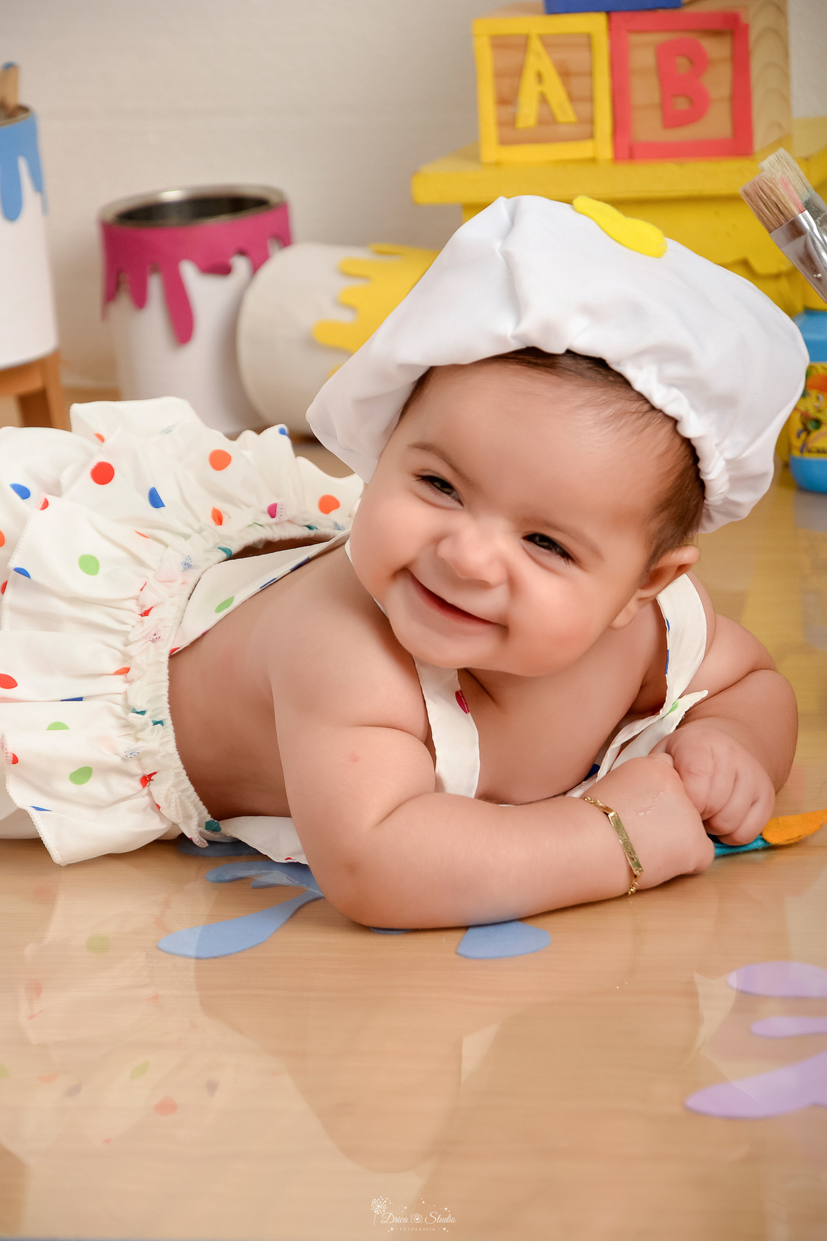 acompanhamento infantil - cenário de aquarela - dia das crianças - mês das crianças - cenários com latas de tintas - bebe deitada sobre o cenário - usando roupinha de pintora e gorrinho na cabeça 