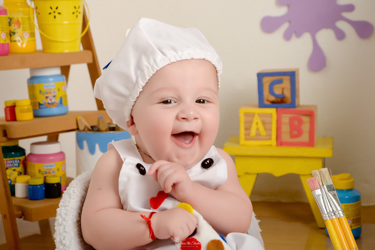 acompanhamento infantil - cenário de aquarela - dia das crianças - mês das crianças - cenários com latas de tintas - bebe usando roupinhas de pintor - marcas de tinta na parede e no chão - pincéis ao lado do bebê - 