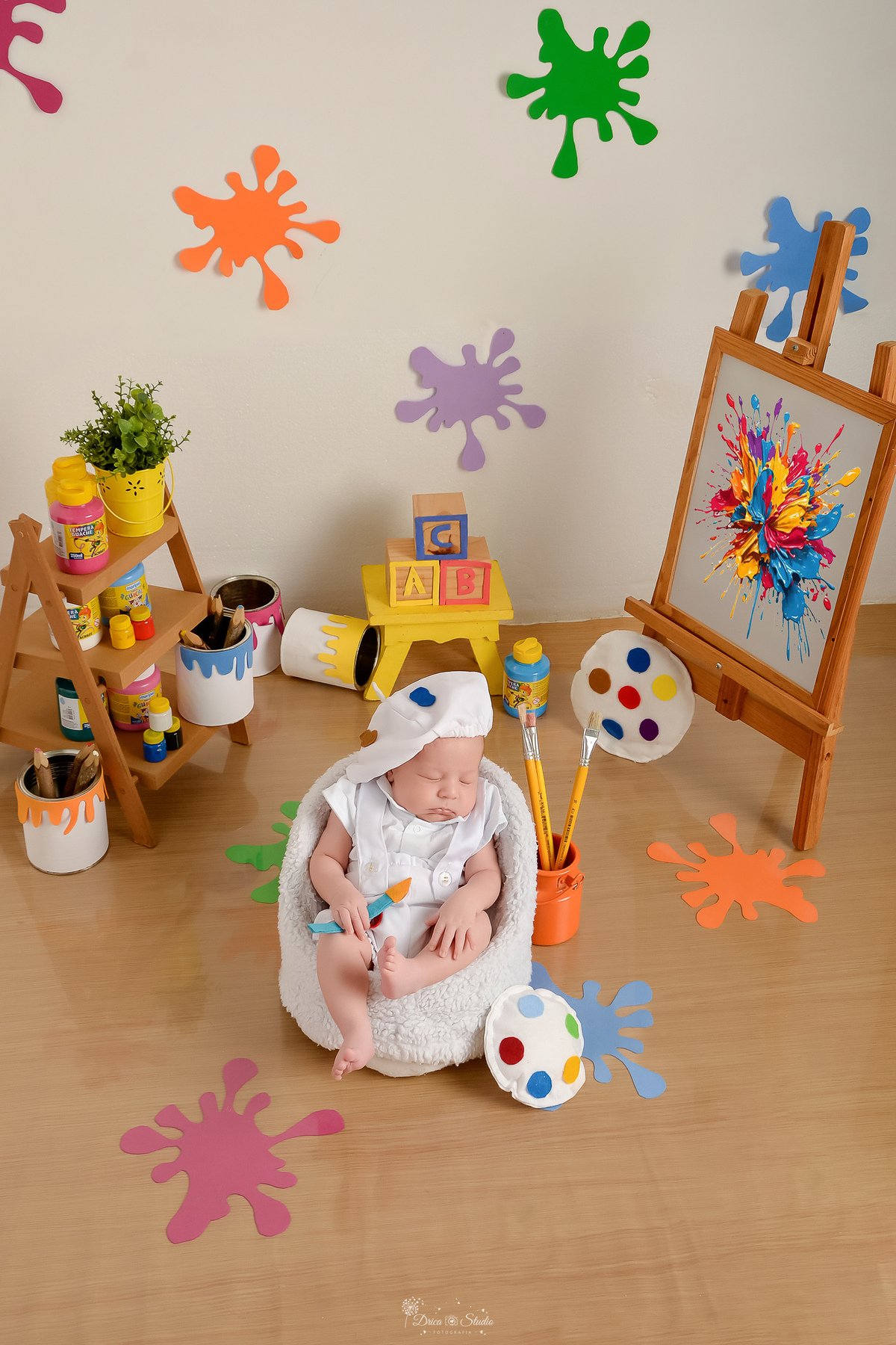 acompanhamento infantil - cenário de aquarela - dia das crianças - mês das crianças - cenários com latas de tintas - bebe dormindo sobre mini sofazinho - segurando pincel de pintura - ao lado lousa com pintura - usando roupinha de pintor e gorrinho 