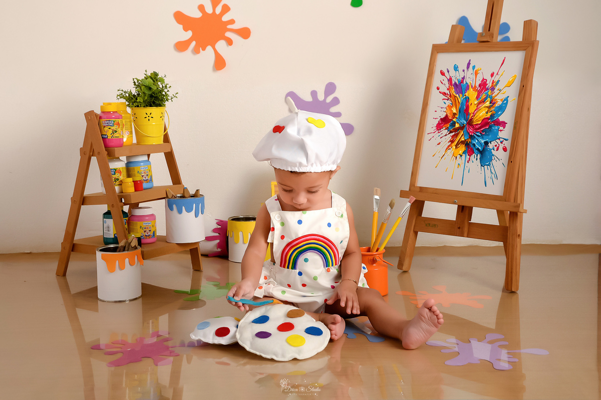 acompanhamento infantil - cenário de aquarela - dia das crianças - mês das crianças - cenários com latas de tintas - bebe sentada no cenário - brincando - usando roupinha de pintora - com gorrinho na cabeça - lousa de pintura - tintas coloridas 