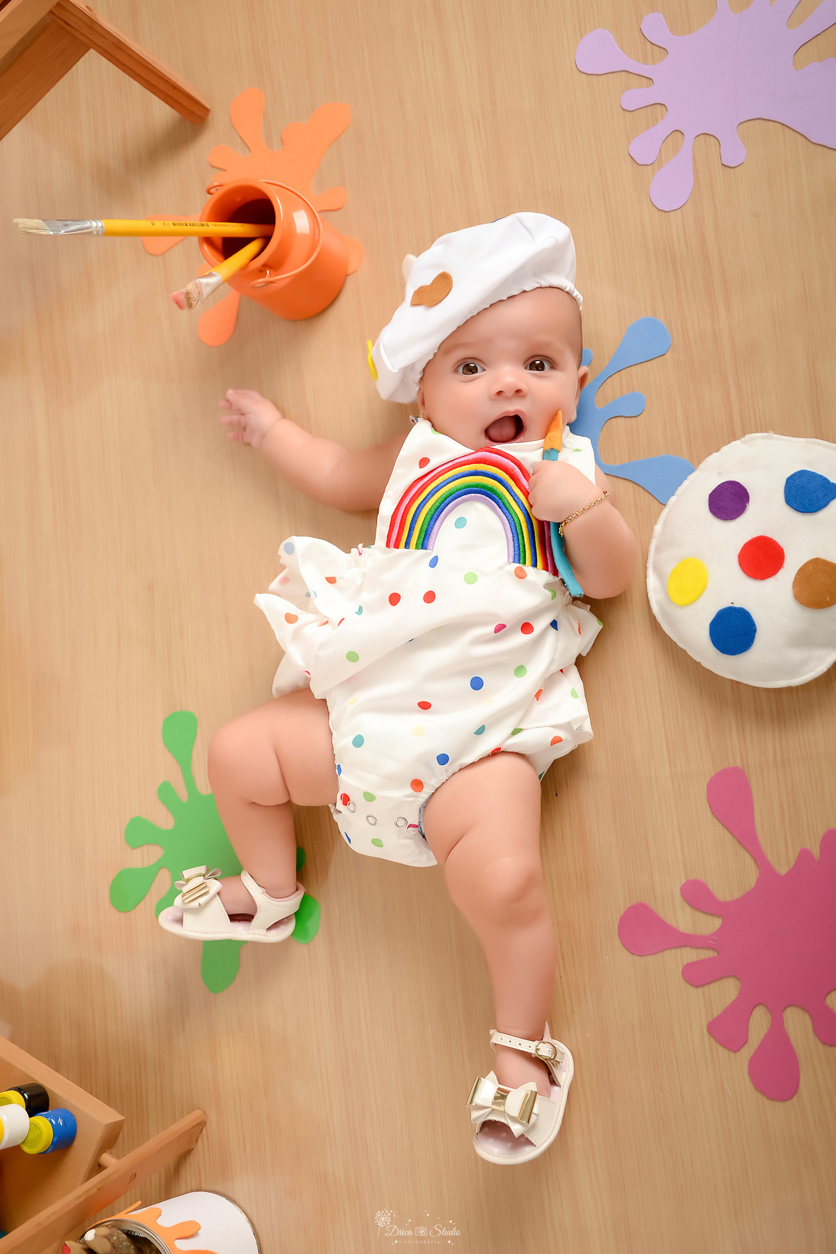 acompanhamento infantil - cenário de aquarela - dia das crianças - mês das crianças - cenários com latas de tintas - bebe deitado sobre o cenário - com pincel de pintura - marcas de tintas coloridas pelo chão - 