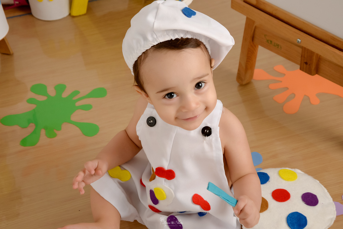 acompanhamento infantil - cenário de aquarela - dia das crianças - mês das crianças - cenários com latas de tintas - bebe usando roupinha de pintor - e gorrinho na cabeça - marcas de tintas coloridas pelo cenario - 