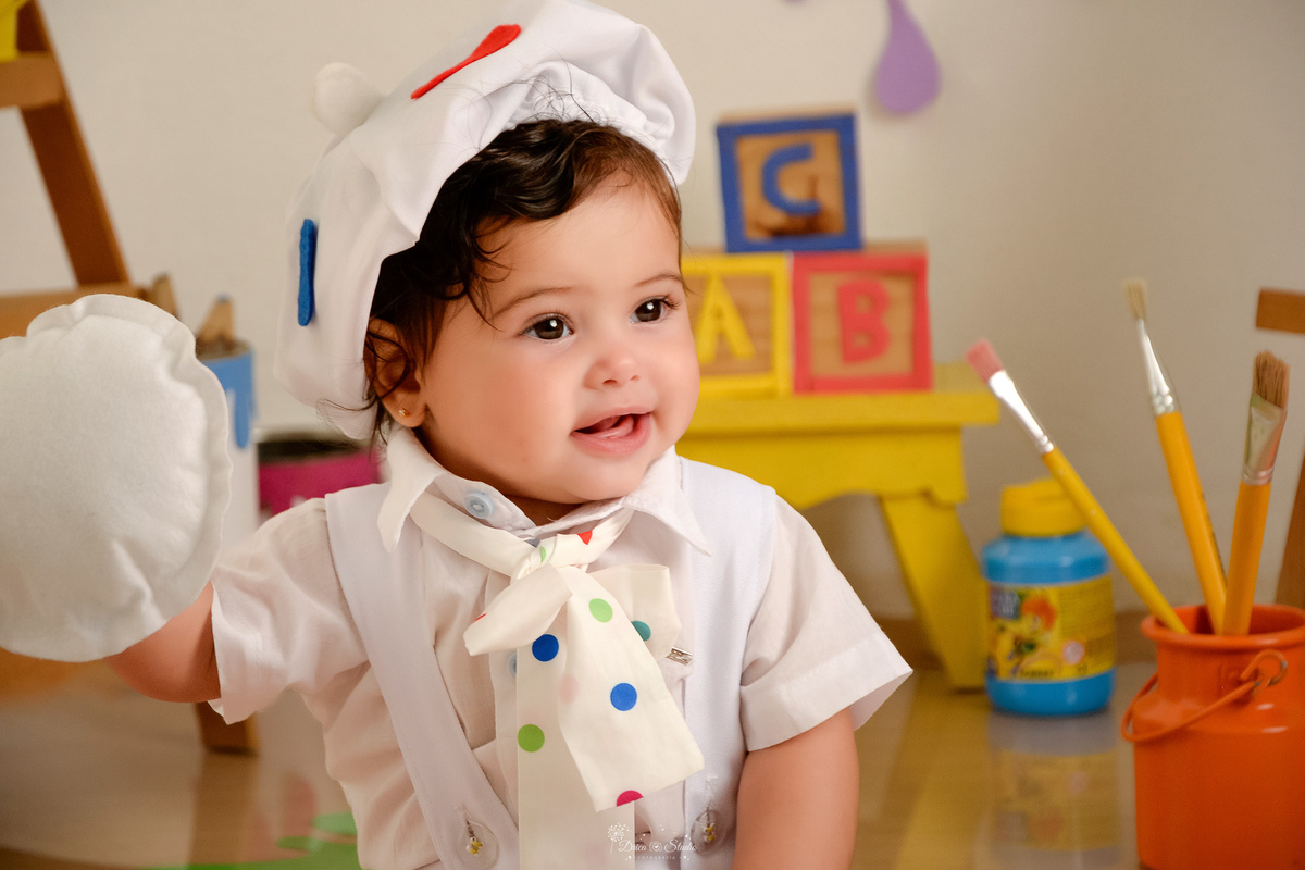 acompanhamento infantil - cenário de aquarela - dia das crianças - mês das crianças - cenários com latas de tintas - bebe usando roupinha de pintura - com gorrinho na cabeça - ao lado lata com pincéis - 