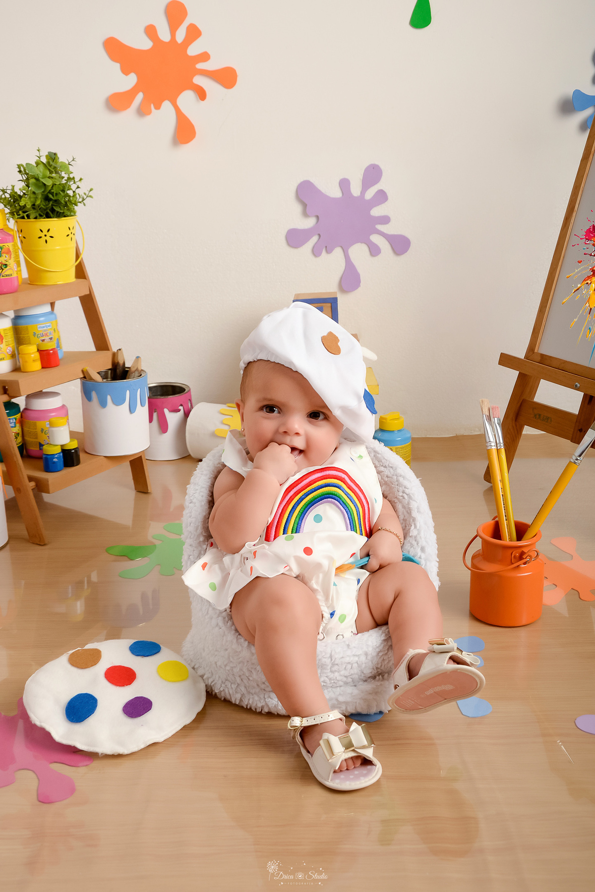 acompanhamento infantil - cenário de aquarela - dia das crianças - mês das crianças - cenários com latas de tintas - bebe usando roupinha de pintor - sentado em mini sofazinho - com a mãozinha na boca 
