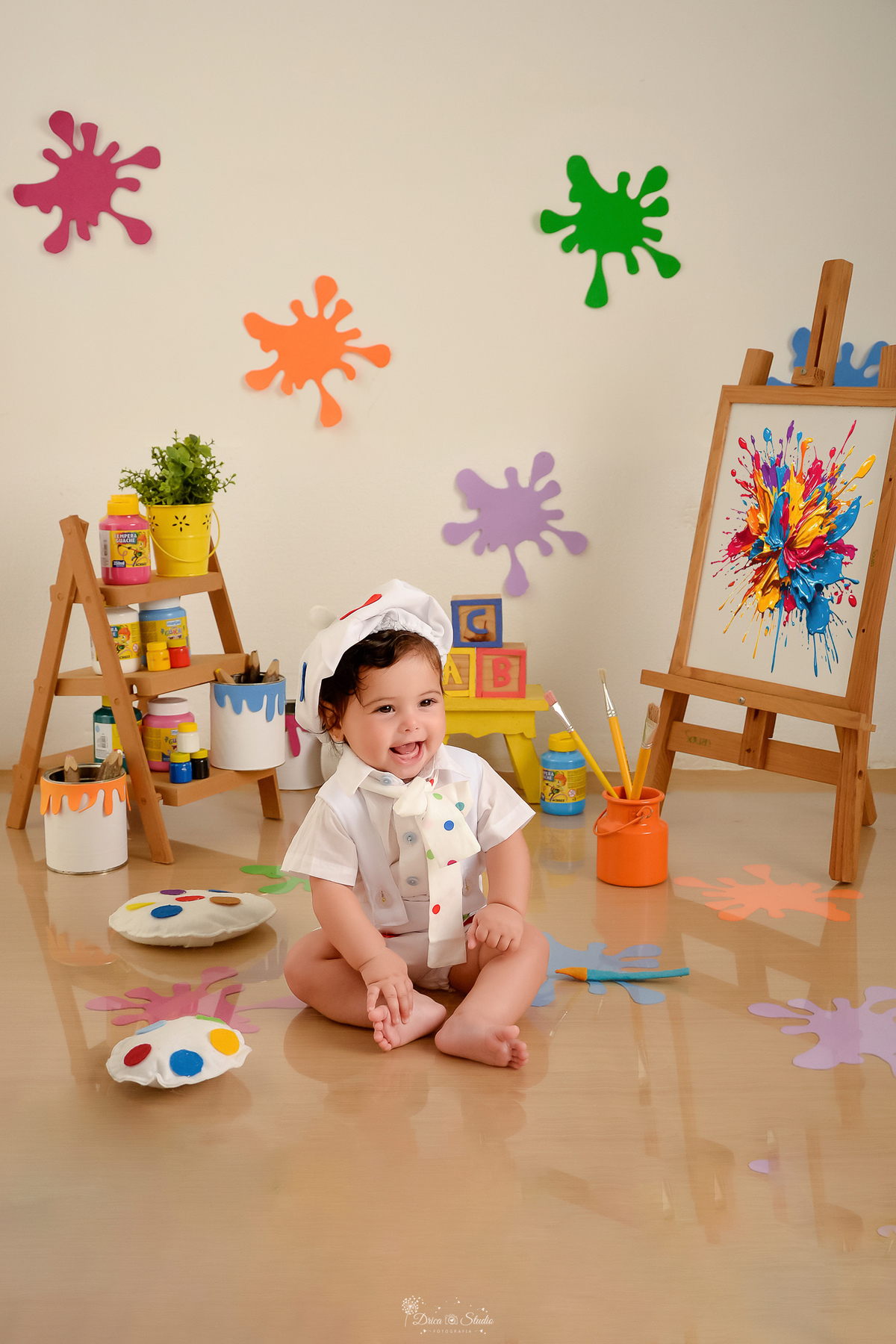 acompanhamento infantil - cenário de aquarela - dia das crianças - mês das crianças - cenários com latas de tintas bebe usando roupinha de pintora com gorrinho na cabeça - marcas de tintas coloridas pelo chão e parede - 