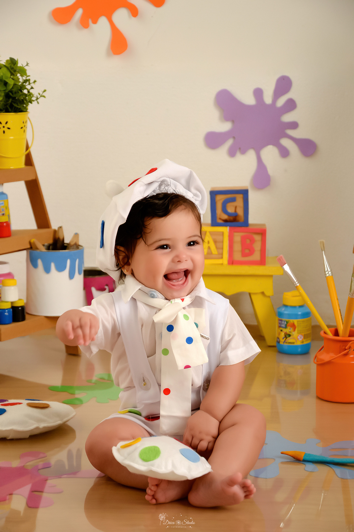 acompanhamento infantil - cenário de aquarela - dia das crianças - mês das crianças - cenários com latas de tintas bebe usando roupinha de pintora com gorrinho na cabeça - sorrindo para a foto 