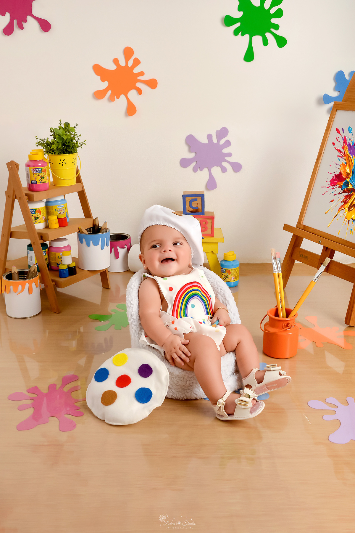acompanhamento infantil - cenário de aquarela - dia das crianças - mês das crianças - cenários com latas de tintas - bebe sentada em mini sofazinho - usando roupinha de pintura  e gorrinho na cabeça - 