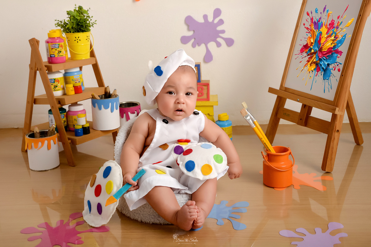 acompanhamento infantil - cenário de aquarela - dia das crianças - mês das crianças - cenários com latas de tintas - bebe usando roupinha de pintor e gorrinho na cabeça - marcas de tintas coloridas pelo cenário - lousa com pintura 