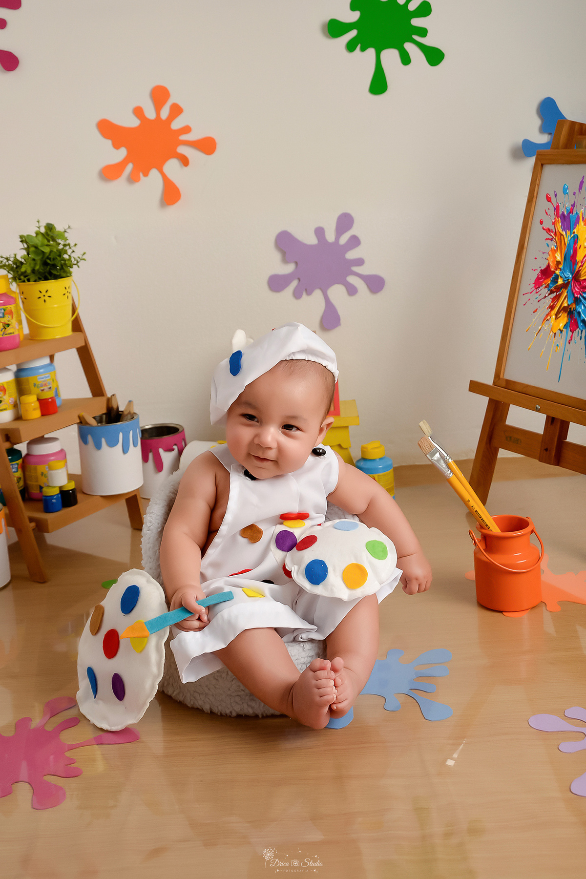 acompanhamento infantil - cenário de aquarela - dia das crianças - mês das crianças - cenários com latas de tintas - bebe sentado em mini sofazinho - segurando pincel de pintura - ao lado de lata de tinta com pinceis 