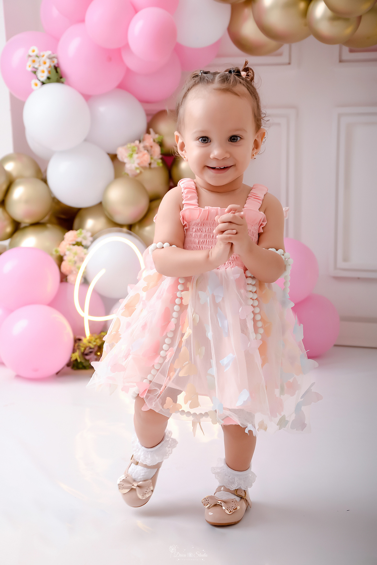 smash the cake - 1 aninho - ensaio infantil - primeiro aninho de vida - cenário com balões nas cores brancos, rosas e dourados - flores pelo cenário - one de led - bebe em pé - usando vestido rosa com boboletas - drica studio - xinguara - pará - 