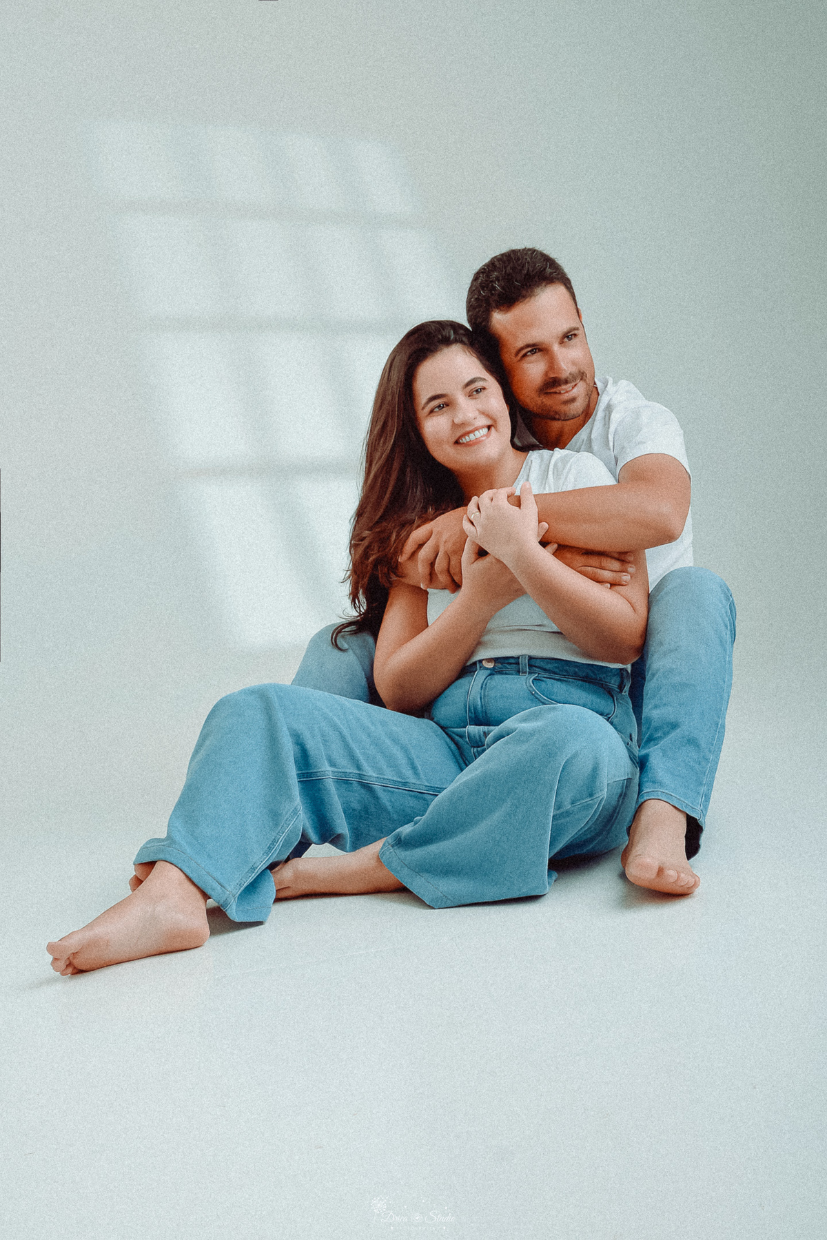 Ensaio casal - ensaio fotografico - fotos em estudio - drica studio - xinguara - pará - casal sentados no chão abraçados - usando camisas brancas e calça jeans - foto com fundo claro - 