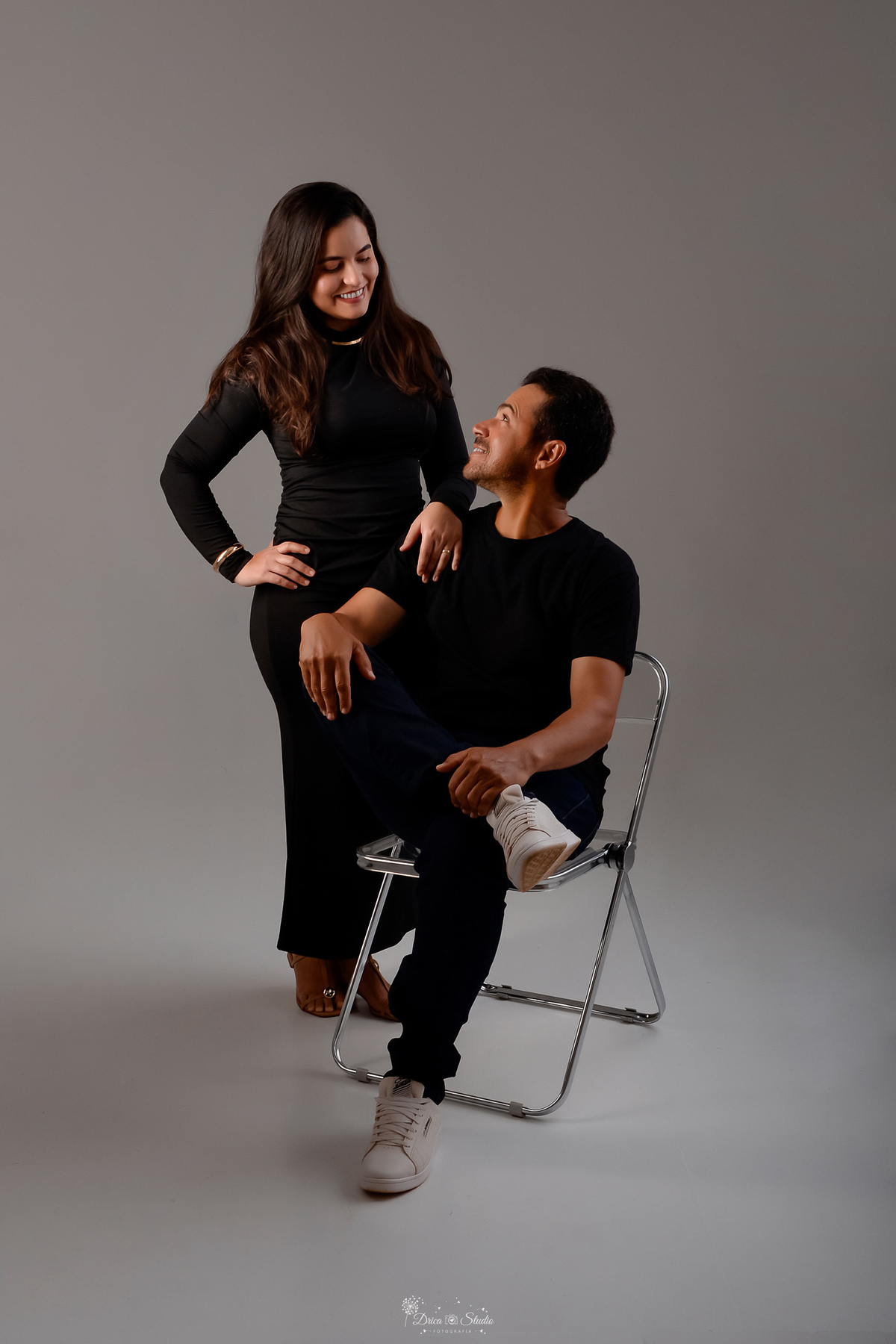 Ensaio casal - ensaio fotografico - fotos em estudio - drica studio - xinguara - pará - casal usando looks na cor preta - ela usando vestido longo de manga na cor preta - ele usando camisa preta e calça jeans - sentado em uma cadeira de meal - 