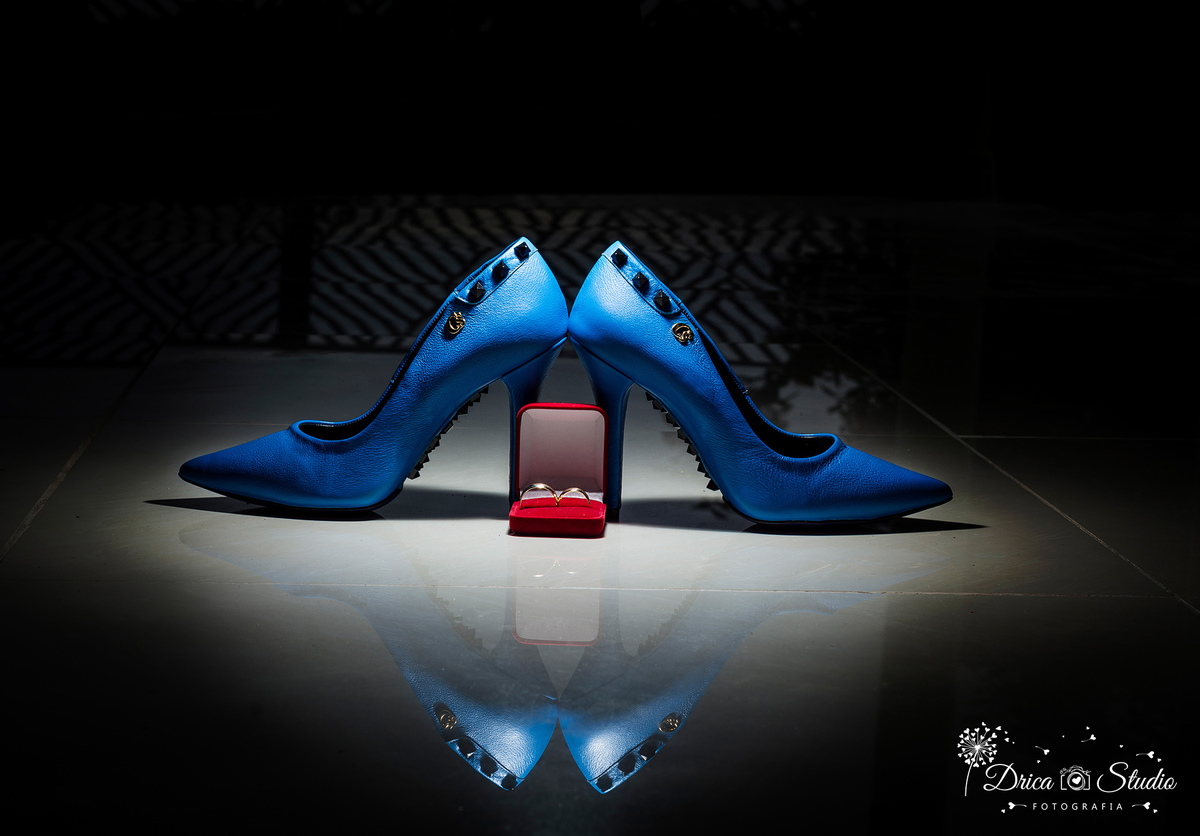 Making off a foto mostra uma imagem dramática de luz dura vindo do alto para o sapatos azul de salto agulha refletindo a imagem no cão, dando um reflexo silhueta escura em volta da foto, e as alianças em uma caixinha vermelha Drica Studio-Casamento