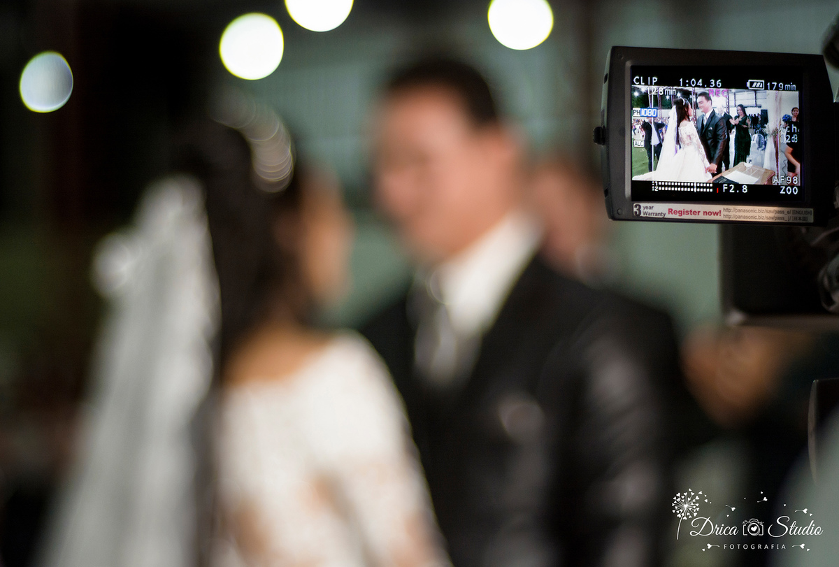foto do visor da câmera de filmagem ao canto da imagem pegando noivo e da noiva peste a se beijarem e em desfoco no resto da foto-Drica Studio-Fotografias-Fotógrafo de Casamento-Xinguara-Pará- Fotografa-Casamento-Sapucaia-Pá.Igreja-Matrimonio.