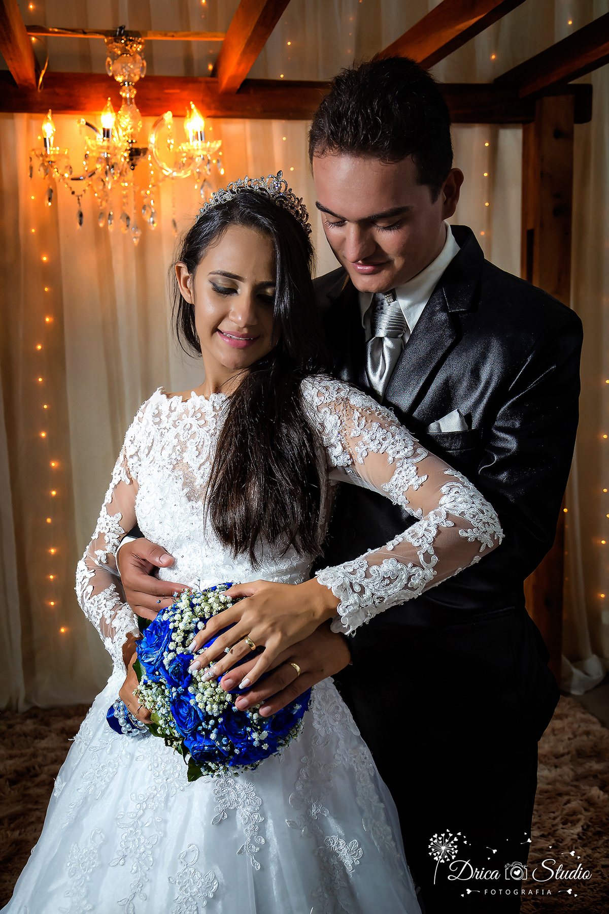noiva e noivos abraçados com as mãos encima do buquê azul da noiva, com as alianças em destaque, ambos estão olhando para as mãos-Drica Studio-Fotografias-Fotógrafo de Casamento-Xinguara-Pará- Fotógrafa- Casamento-Sapucaia-Pá-Cerimonia-Igreja-casal-noivos