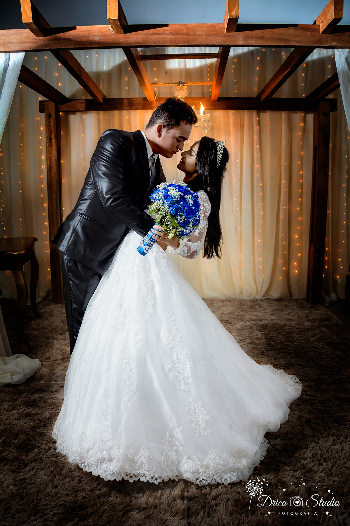 foto clássica onde o noivo deita a noiva como se fosse beijá-la o vestido branco faz um movimento e ao fundo uma costina de luz. -Drica Studio-Fotografias-Fotógrafo de Casamento-Xinguara-Pará- Fotografa-Casamento-Sapucaia-Pá.Casal-beijo-pisca-pisca.