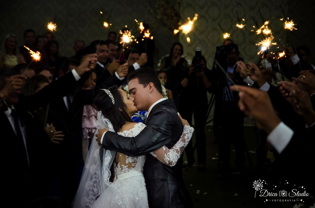 foto mostra noivos beijando entre arco de fogos feitos pelos padrinhos.Drica Studio-Fotografias-Fotógrafo de Casamento-Xinguara-Pará- Fotografa- Making of-Casamento-Sapucaia-Pá.Beijo- noivos-Casal- Fogos-Festa- Casamento-Cerimonia-Amor-casados-passarela.