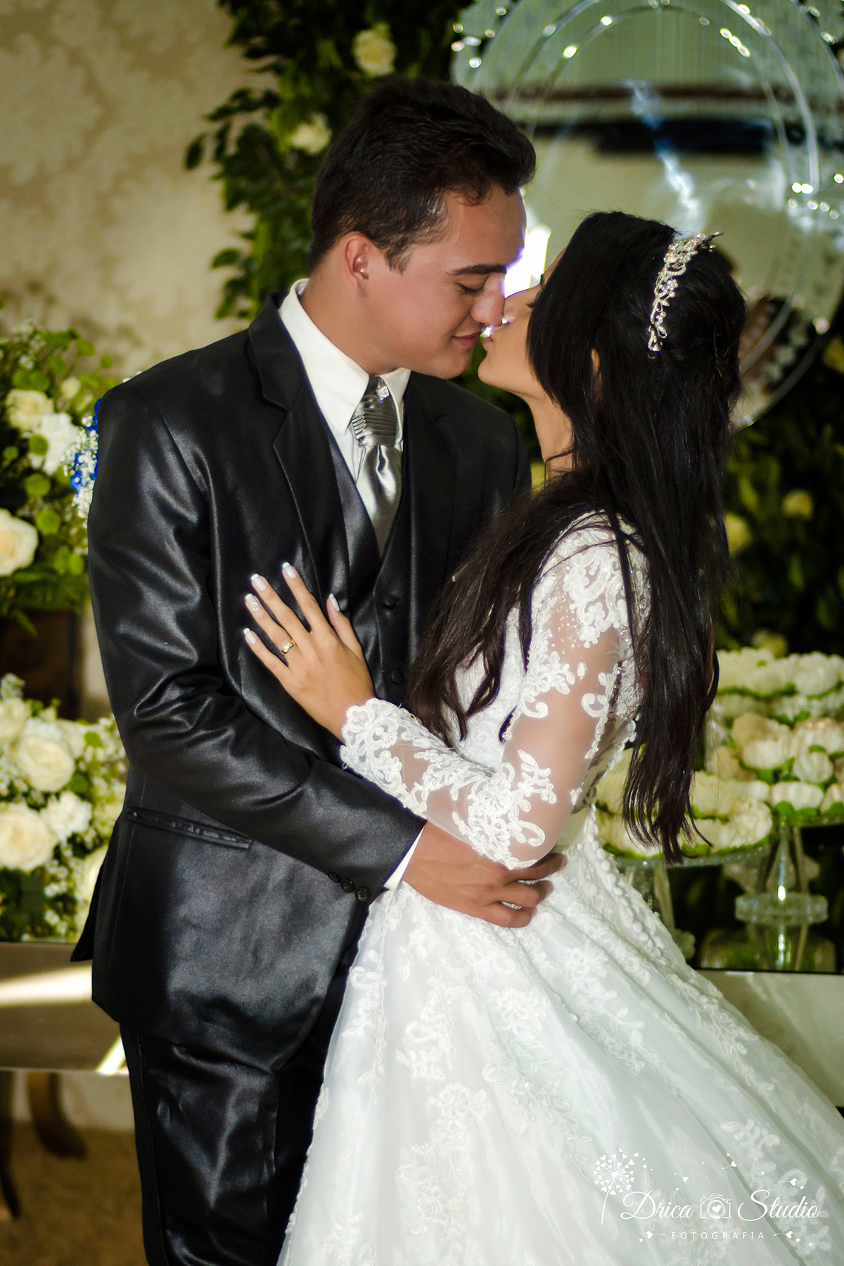 Foto da noiva e o noivo se beijando abraçados e ao fundo-uma linda decoração da festa folhas verde com flores brancas-Drica Studio-Fotografias-Fotógrafo de Casamento-Xinguara-Pará- Fotógrafa- Casamento-Sapucaia-Pá-Cerimonia-Igreja-lindo-casal--beijando.