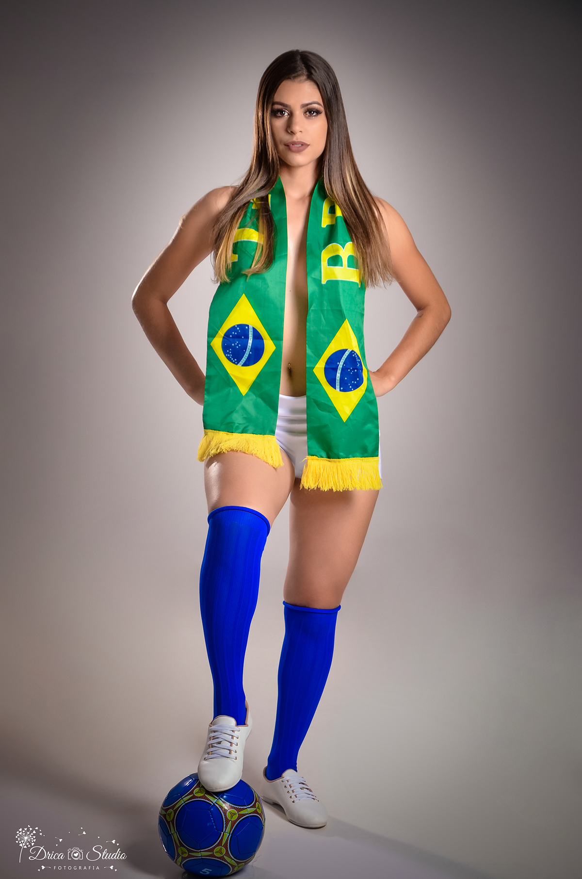 Drica Studio- Fotografias- Fotógrafo-Xinguara-Pará- Fotografa- Estúdio-ensaio-Feminino-Copa do Mundo- Brasil.foto de ensaio onde a modelo cobre os seios com faixa verde do brasil, mãos na cintura e com o pé na bola. 